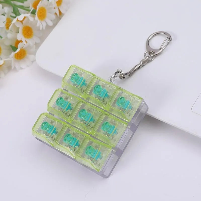 A clear plastic keychain featuring multiple green silicone clicking buttons attached to a silver keyring.