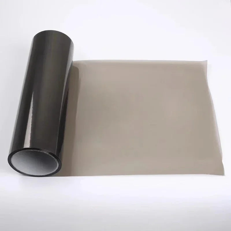 Roll of smoke black headlight and taillight tint film displayed next to a rectangular piece of tinted plastic.