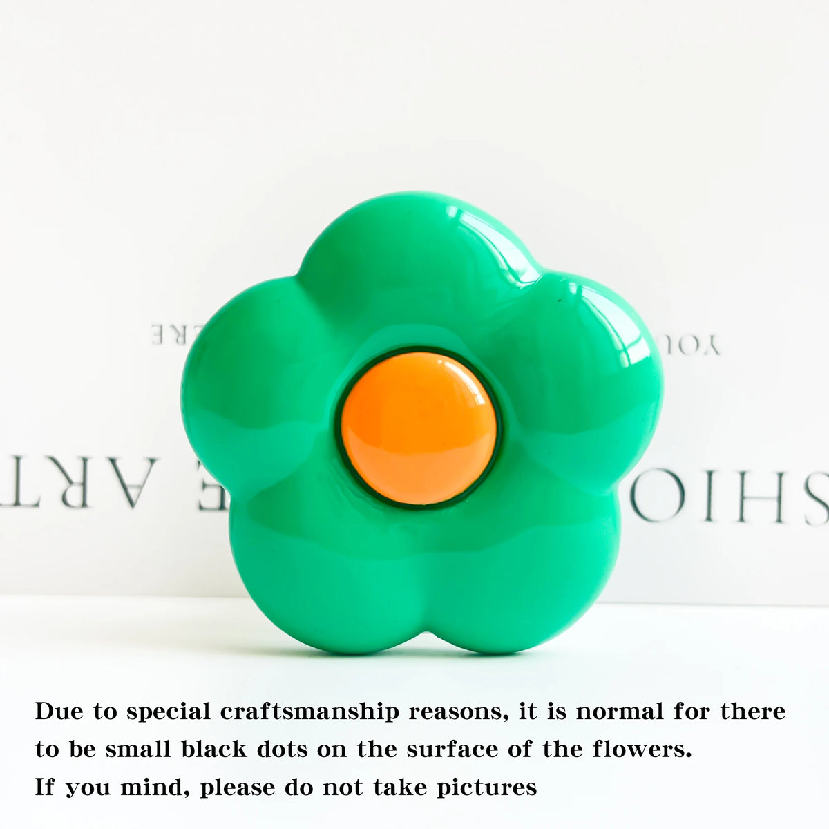 A vibrant green flower-shaped phone grip stand with an orange center and small black dots on the surface.