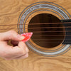 A hand is holding a pink guitar pick above an acoustic guitar fretboard.