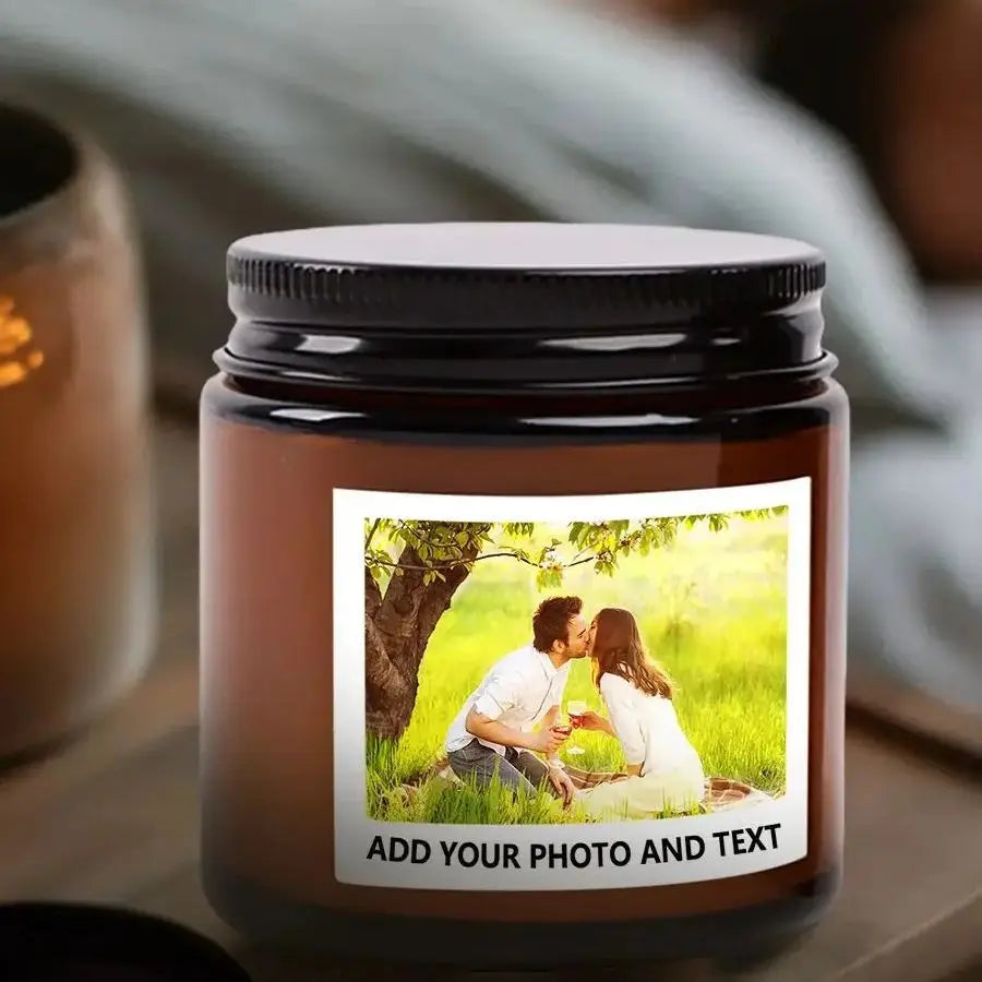 A dark brown soy candle in a glass jar with a photo and text insert, set on a wooden surface.