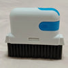 A white and blue multi-purpose crevice cleaning brush with black bristles resting on a light pink surface.