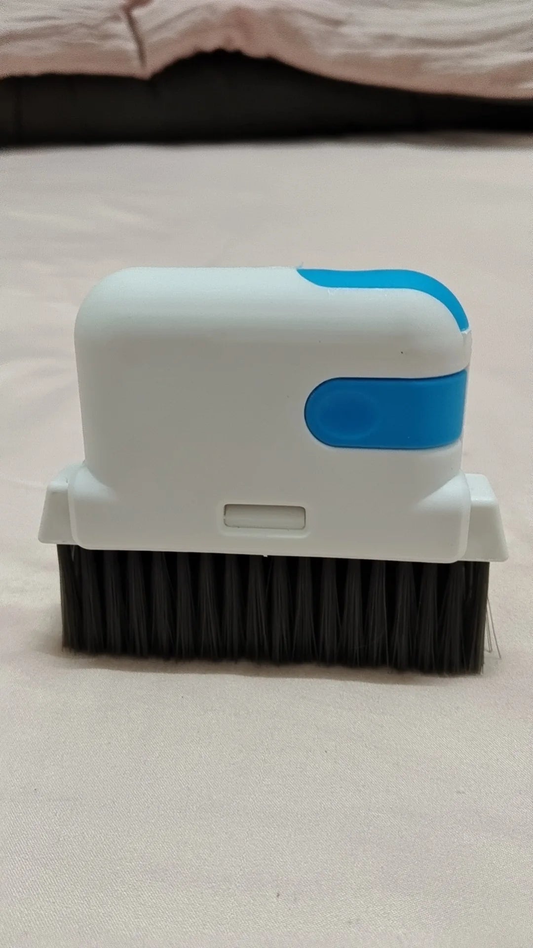 A white and blue multi-purpose crevice cleaning brush with black bristles resting on a light pink surface.