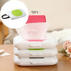 A stack of white refillable wipe dispensers with pink and lime green accents on a wooden surface.