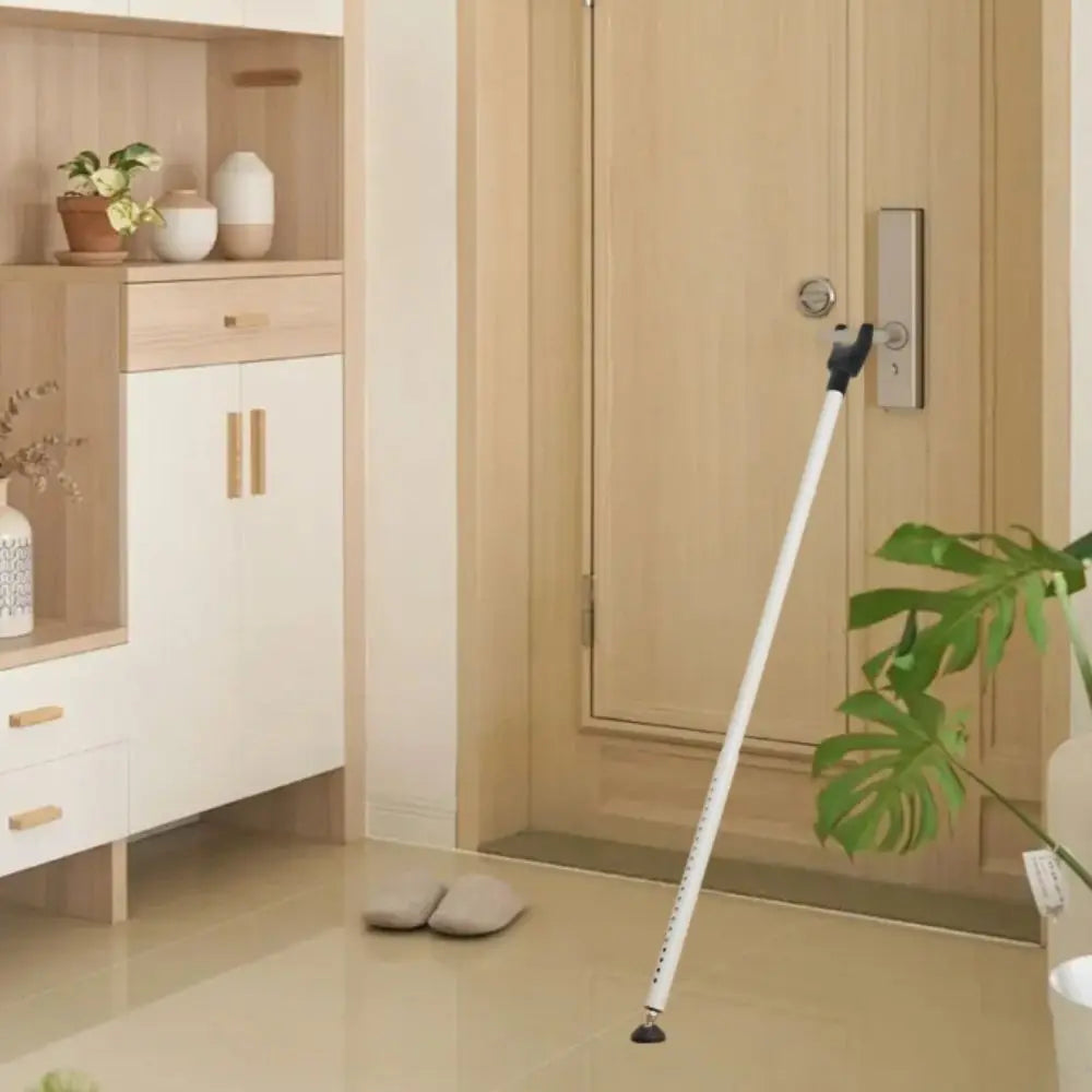A white adjustable door security bar is shown next to a light wood cabinet and a beige door.