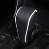 Close-up of a black leather gear shift knob cover with white trim, shown in a dark interior context.