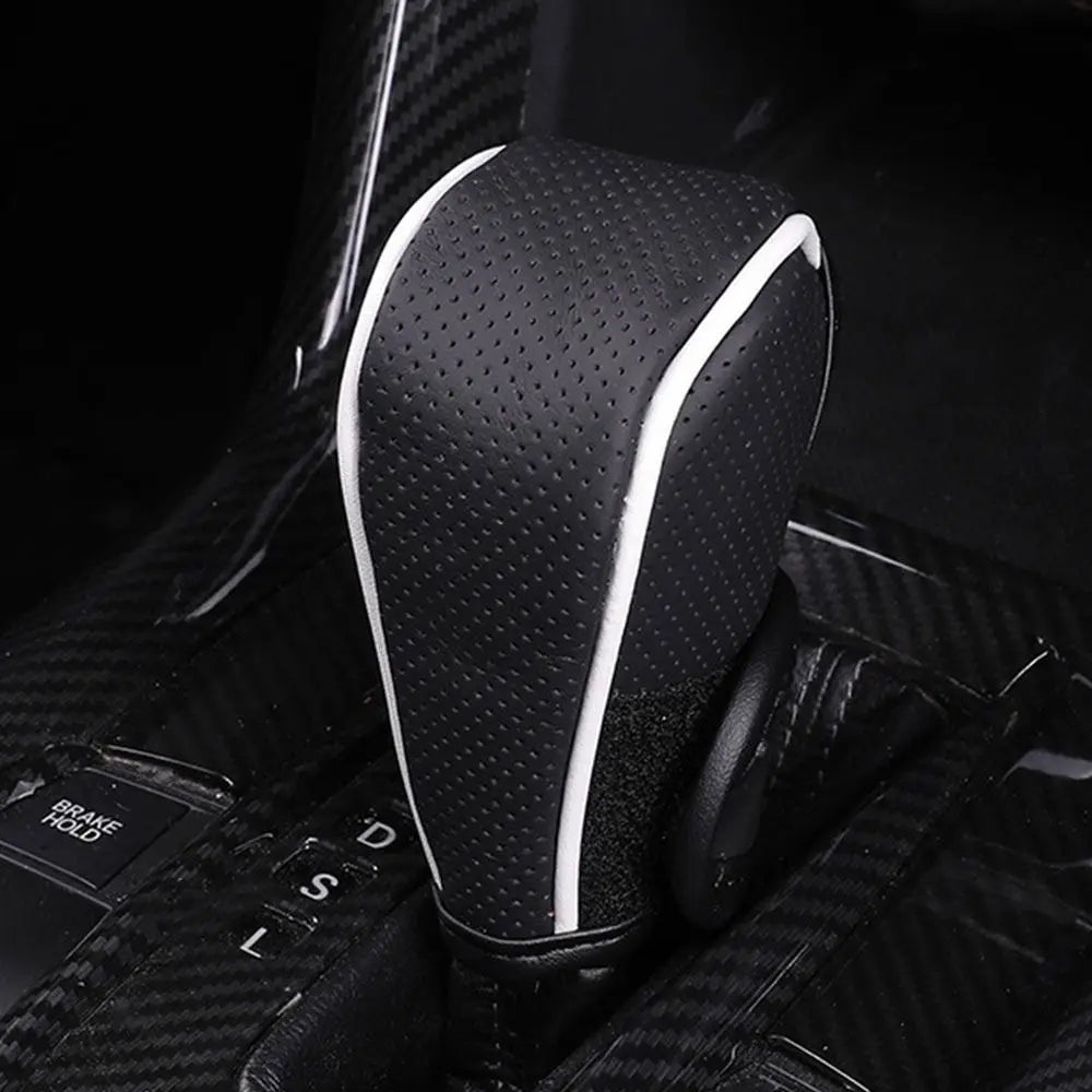 Close-up of a black leather gear shift knob cover with white trim, shown in a dark interior context.