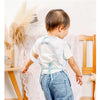 A toddler wearing a white waterproof full-body feeding bib with a sleeveless design and denim overalls.
