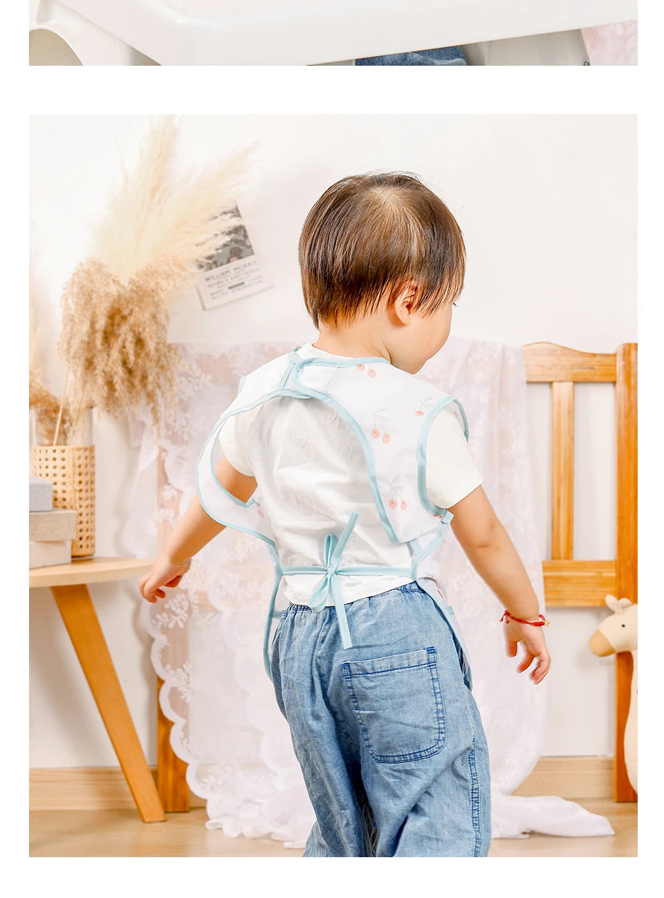 A toddler wearing a white waterproof full-body feeding bib with a sleeveless design and denim overalls.
