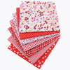 A bundle of red, white, and pink cotton fabric squares featuring various floral, dot, and plaid patterns for patchwork.