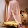 A romantic pink mosquito net canopy draped over a double bed with sheer fabric and string lights.