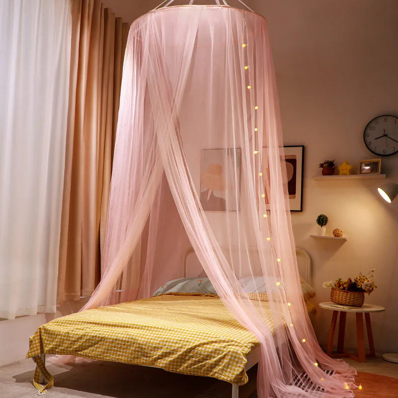A romantic pink mosquito net canopy draped over a double bed with sheer fabric and string lights.