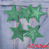 A set of five green glitter star iron-on embroidered patches placed on a denim fabric.