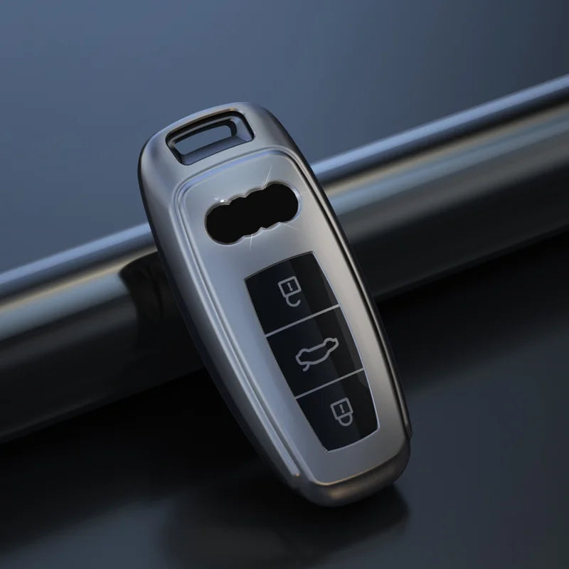 Titanium gray Audi key fob cover with a clear window and three buttons resting on a dark surface.