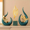 A set of three gold and teal ceramic sculptures featuring stylized leaf shapes on a light wood surface.