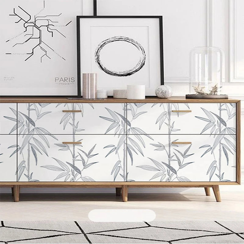 A wooden dresser with white drawers featuring a botanical leaf pattern and a framed artwork.
