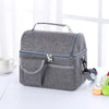 A gray insulated lunch bag with a handle and zippered compartments is shown on a white surface.