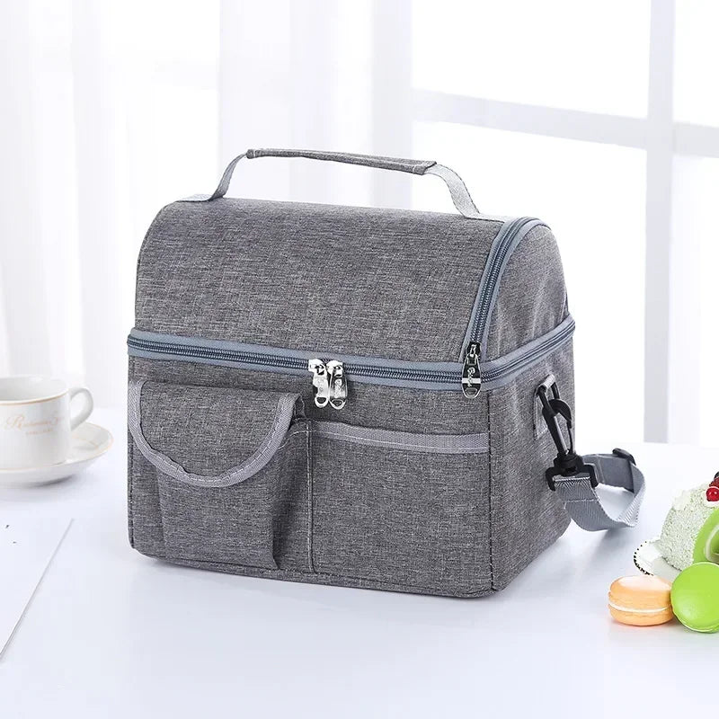 A gray insulated lunch bag with a handle and zippered compartments is shown on a white surface.