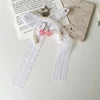 A pearl bow keychain with a heart charm and white lace ribbon displayed on a light background.
