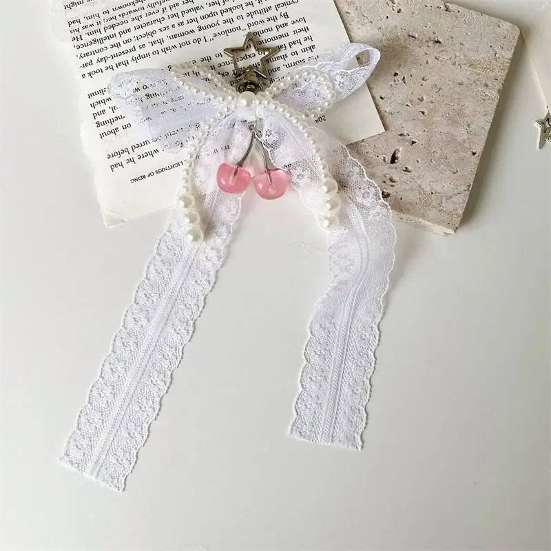 A pearl bow keychain with a heart charm and white lace ribbon displayed on a light background.