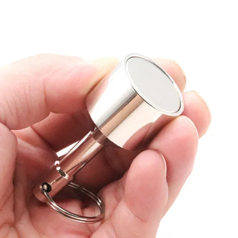 A hand holds a silver-colored neodymium magnet keychain with a detachable clasp.