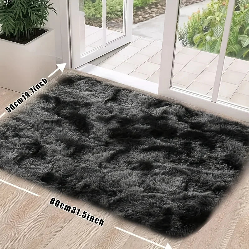 A rectangular dark gray plush silk-touch area rug placed on a light wood floor near a glass door.