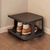 A dark gray stackable vertical shoe rack holding pairs of brown and tan boots on a wooden floor.