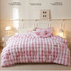 A pink and white checkered plush winter comforter is displayed on a bed with light wood accents.