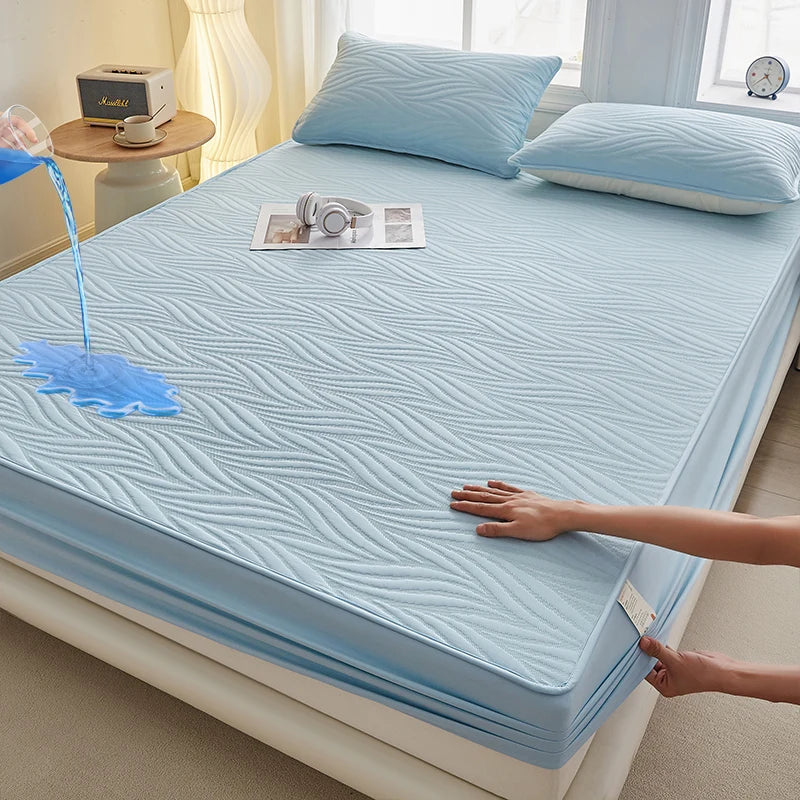 A light blue floral waterproof fitted mattress protector is displayed on a bed, with a hand touching the fabric.