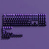 A close-up photo of a purple PBT double-shot keycap set with gradient colors displayed on a dark surface.
