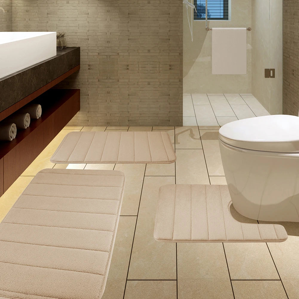A set of beige plush memory foam bath mats with non-slip backing placed on a tiled bathroom floor.