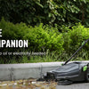 A person is operating a black walk-behind push floor sweeper outdoors on a paved surface.