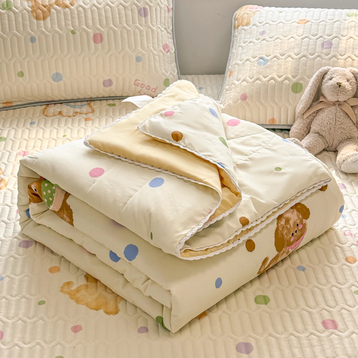 A stack of cream colored lace-trim breathable summer duvet covers and pillows on a quilted surface.