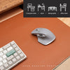 A gray ergonomic computer mouse resting on a brown leather desk mat with office and furniture icons in the background.