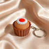 A small, round cake-shaped fidget keychain with white frosting and an orange center, resting on silky pink fabric.