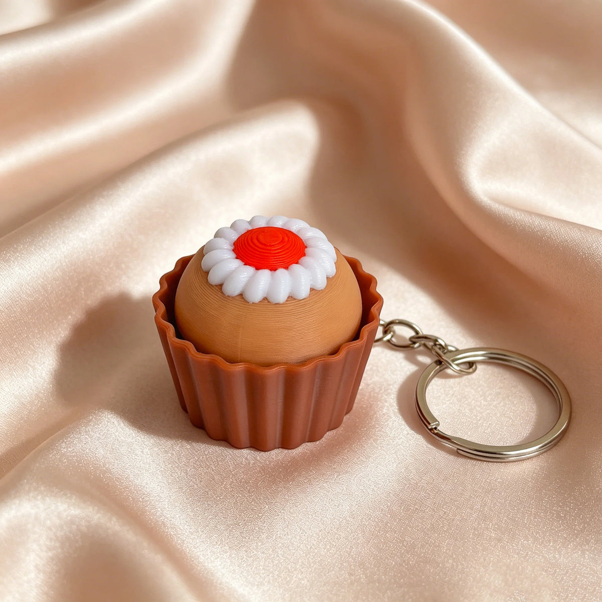 A small, round cake-shaped fidget keychain with white frosting and an orange center, resting on silky pink fabric.