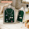 Silver arched resin jewelry display stand with a dark green velvet lining showcasing various necklaces and earrings.