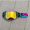A pair of bright yellow and black motocross goggles with pink accents resting on a gray paved surface.