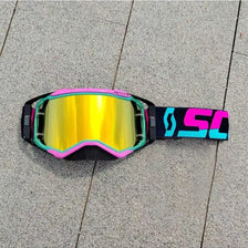 A pair of bright yellow and black motocross goggles with pink accents resting on a gray paved surface.