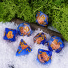 A set of adorable animal resin dice in blue and gold colors resting on white snow with green moss in the background.