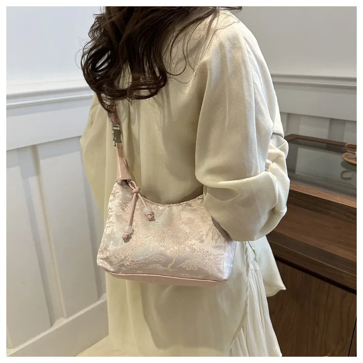 Eine Frau hält eine hellrosa Perlenstickerei-Crossbodytasche gegen ein weißes, fließendes Kleidungsstück.
