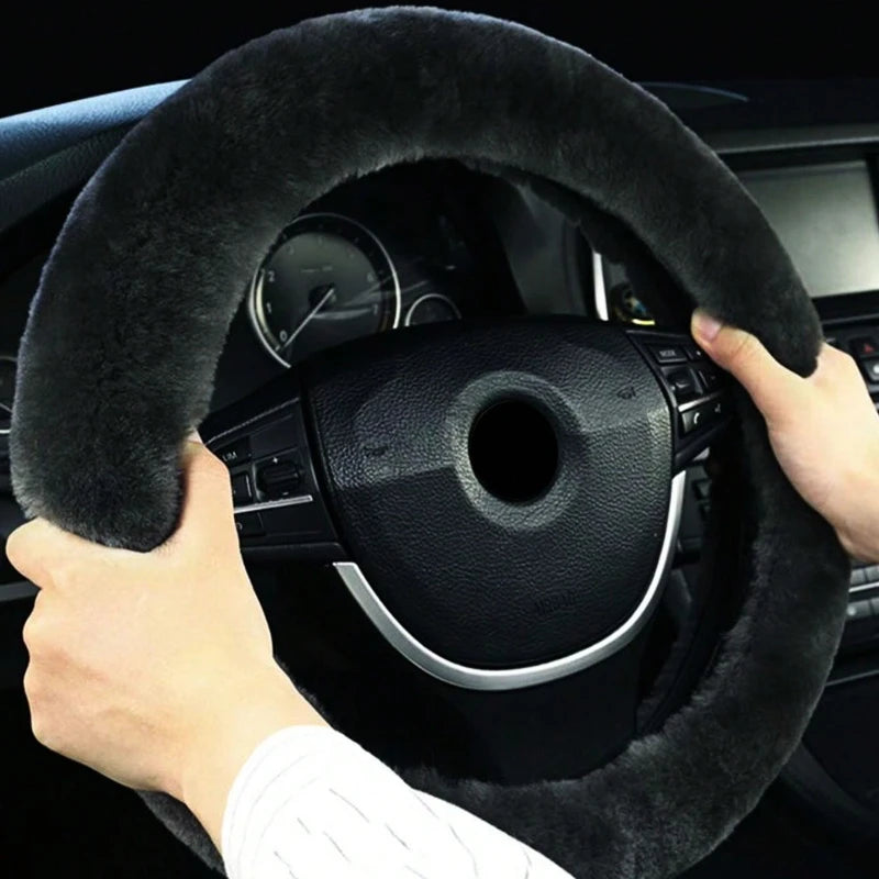 A hand grips a black winter plush steering wheel cover on a car interior.