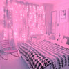 A bedroom decorated with pink LED curtain string lights illuminating sheer curtains and a bed.