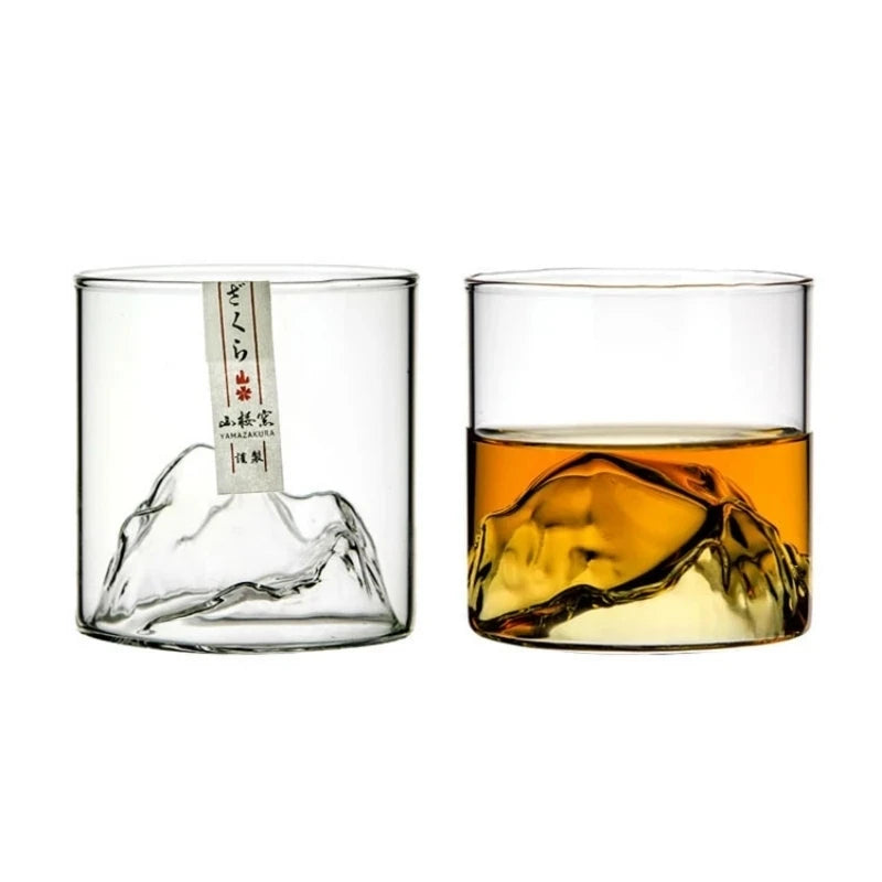 A clear whiskey glass filled with amber-colored liquid, showing a mountain ice cube shape.