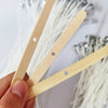 A hand holds three natural cotton candle wicks with metal stands against a white background.