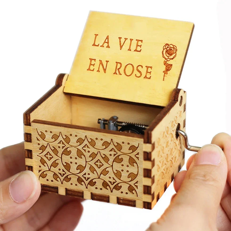 A wooden music box with a lid engraved LA VIE EN ROSE is held in a hand.