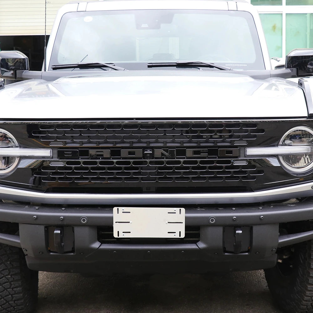 Close-up of a black Ford Bronco grille with a white emblem letter cover installed on the front bumper.