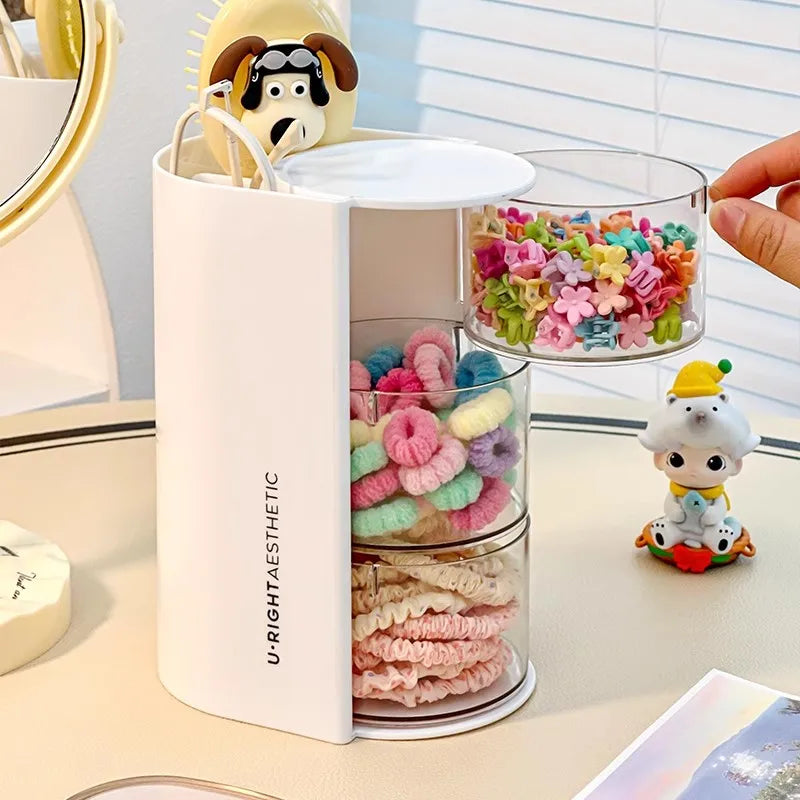 Clear acrylic hair accessories organizer with rotating compartments holding colorful hair ties and accessories.
