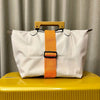 A white reusable elastic luggage strap with an orange strap and a wooden handle resting on a yellow surface.