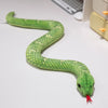 A bright green lifelike snake plush toy with a red tip is coiled on a white surface.